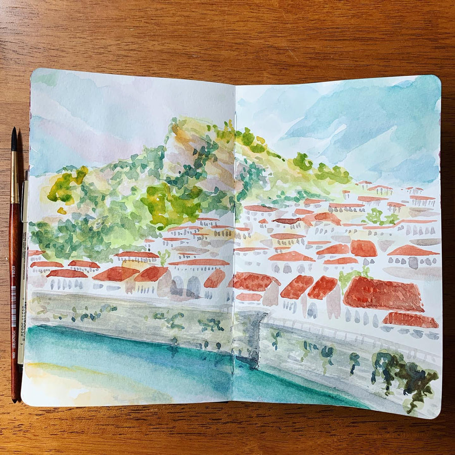 sketchbook watercolor of a hillside town with red roofs