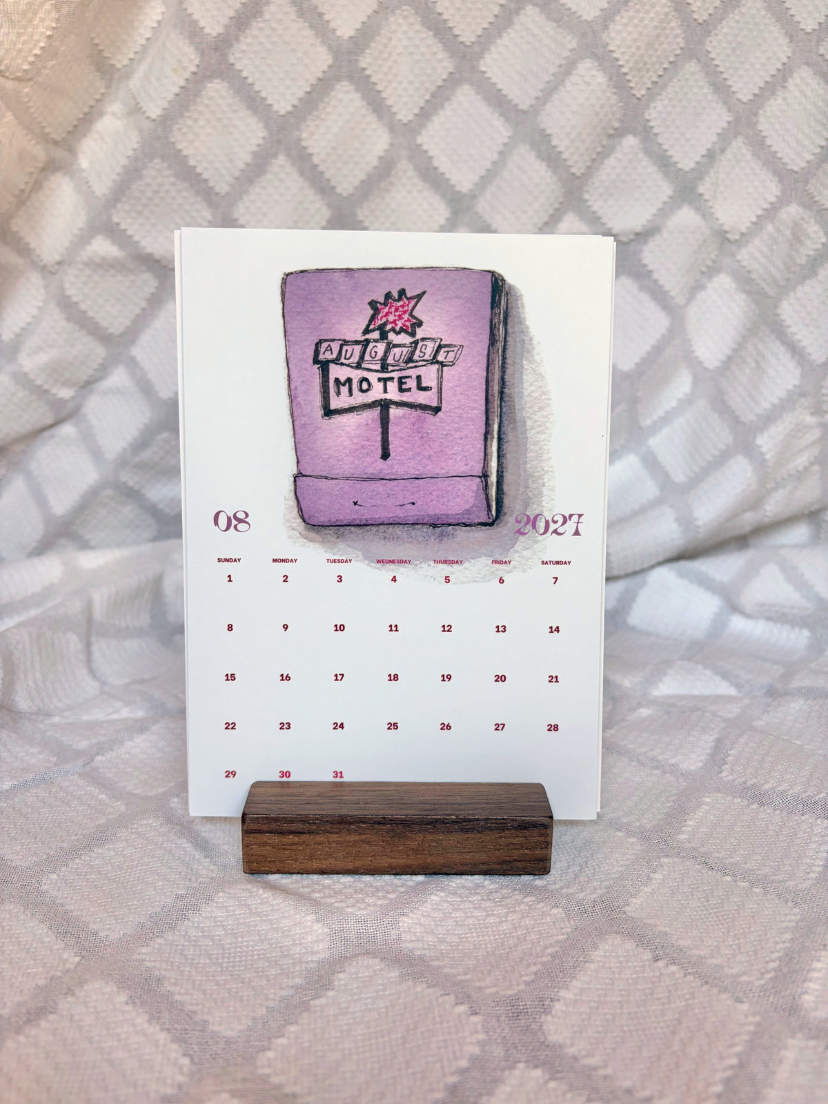 august 2027 postcard calendar card with purple motel matchbook on wood stand