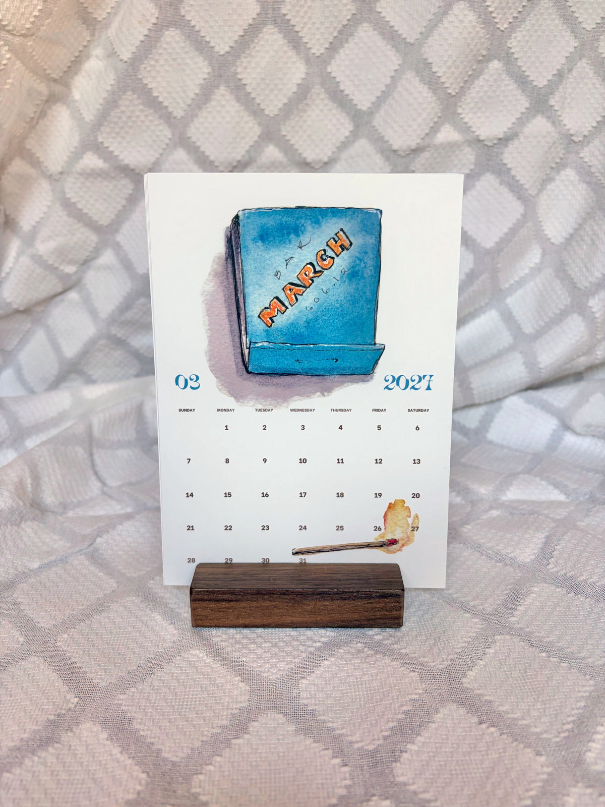 march 2027 postcard calendar card with blue watercolor matchbook on wood stand
