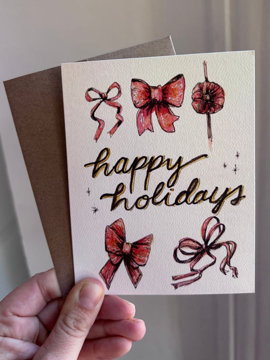 happy holidays bows watercolor greeting card by arthus, held in hand with a kraft envelope